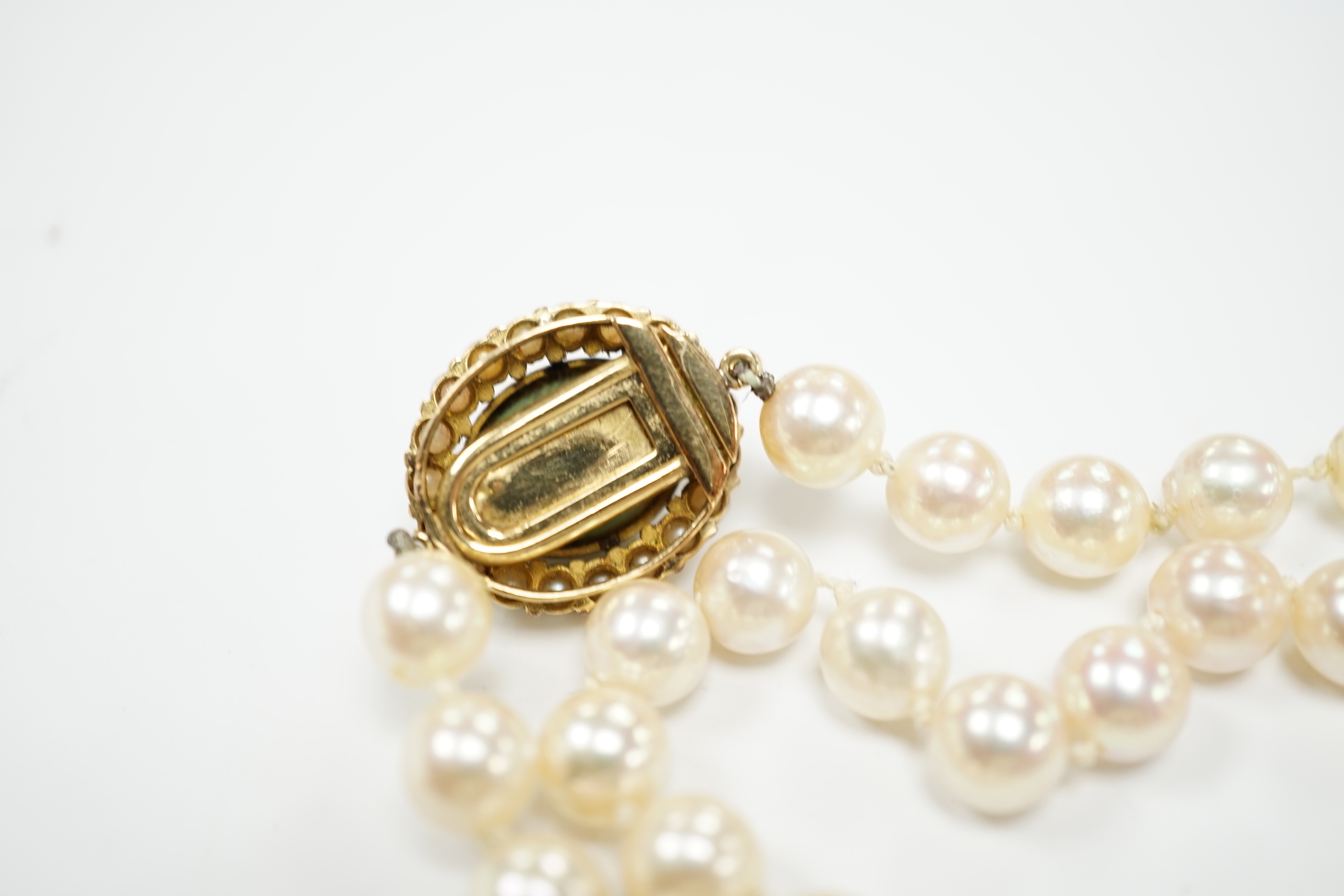 A Portuguese single strand cultured pearl necklace, with cabochon nephrite and seed pearl cluster set yellow metal clasp, 86cm.